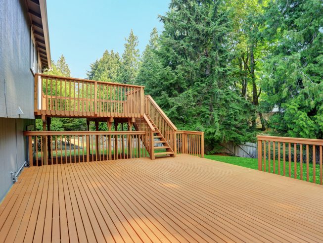 Backyard view of grey rambler house with upper and lower decks and green lawn. Kirkland, WA, USA.